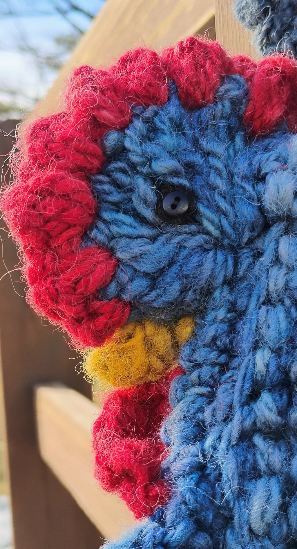 Close-up of crocheted hen face with red comb, yellow beak, and glass eye on handspun wool bag