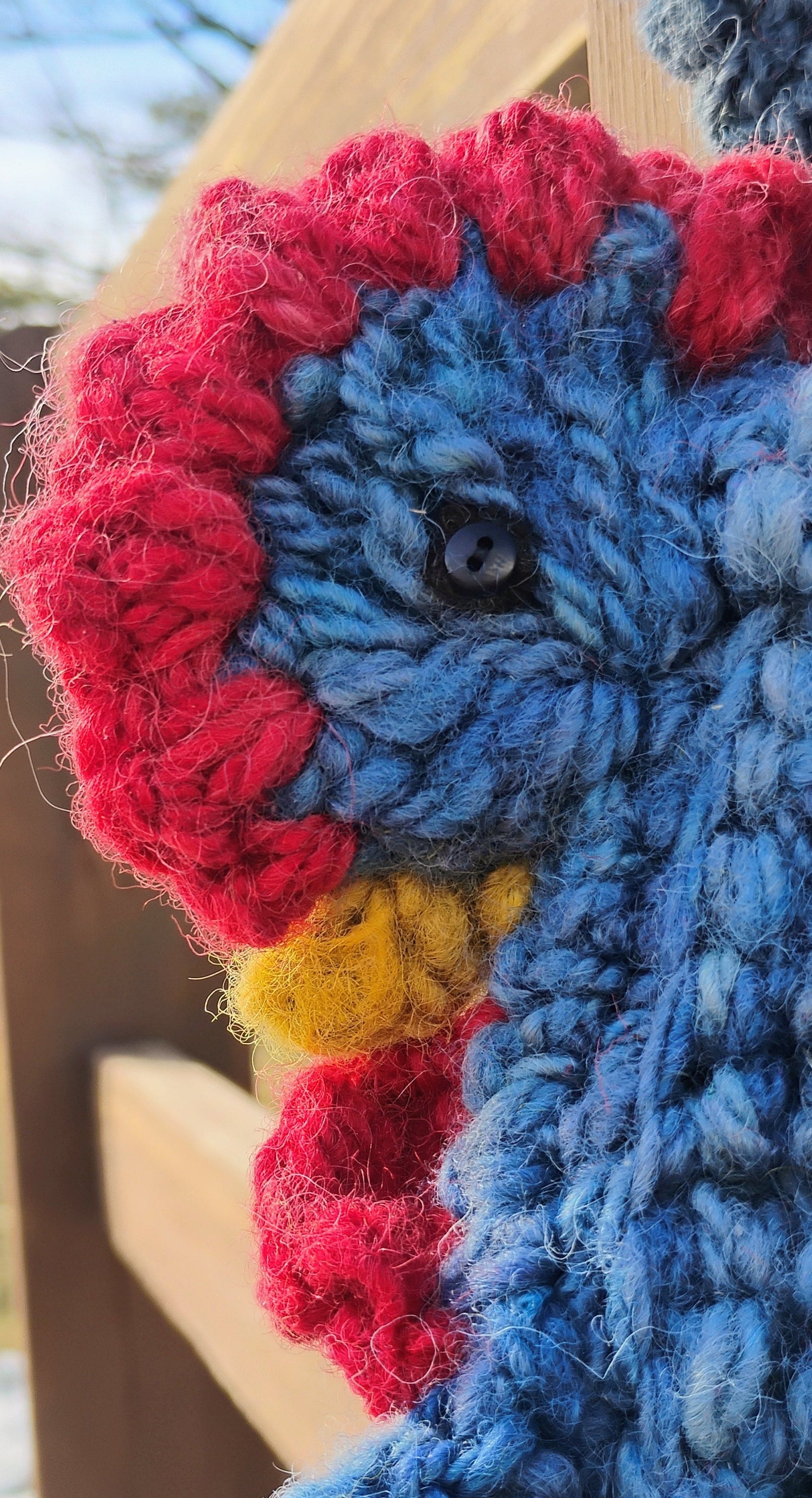 Close-up of crocheted hen face with red comb, yellow beak, and glass eye on handspun wool bag